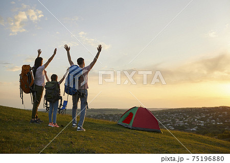 Family camping in nature. Parents and child with backpacks enjoying beautiful sunset at campground, copy space Family camping in nature. Parents and child with backpacks enjoying beautiful sunset at campground, copy space 75196880
