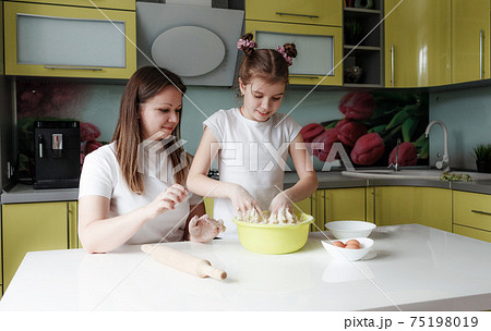 Young mother and daughter together prepare dough in the kitchen Young mother and daughter together prepare dough in the kitchen 75198019