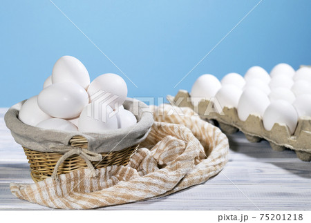 White Chicken eggs in a cardboard box and in a Straw basket on a light blue background with piece of cloth, Raw Fresh Chicken Eggs in a paper container, Natural Product 75201218