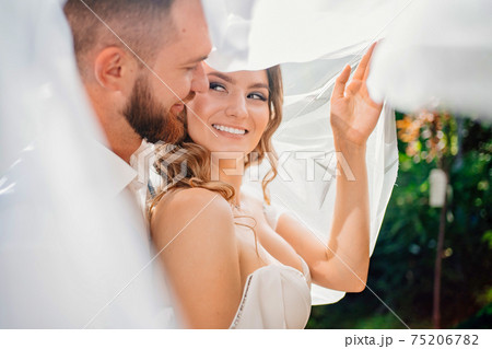 under the veil Happy and beautiful bride and groom gently cuddle in the park under the veil Happy and beautiful bride and groom gently cuddle in the park 75206782