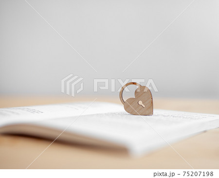 A wooden heart with a keyhole rests on an open book. 75207198