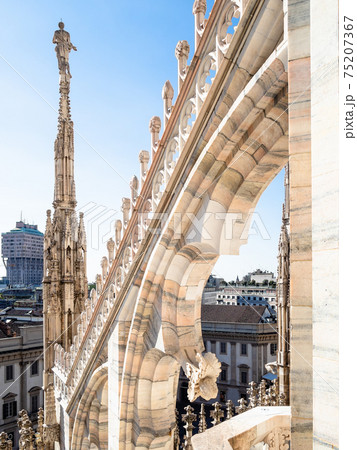statue on spire of Duomo di Milano roof over city 75207367