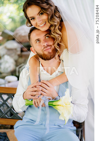 the bride with long curls gently hugs shoulders the groom in a blue suit 75208484