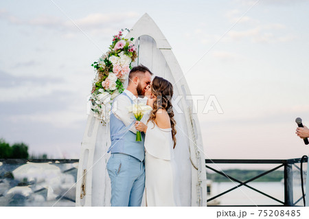 happy newlyweds kiss. beautiful wedding ceremony by water on dock.  75208485