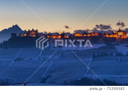Italy Piedmont: panoramic winter snow view wine yards unique landscape at sunset, medieval castle and village on hill top, the Alps in the background dramatic sky Italy Piedmont: panoramic winter snow view wine yards unique landscape at sunset, medieval castle and village on hill top, the Alps in the background dramatic sky 75209382