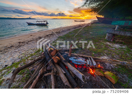 Fish bbq on tropical desert beach. Cooking barbecue with wood fire at sunset, colorful sky on sea, dramatic clouds, getting away, adventure in Indonesia Sumatra Banyak Islands 75209406