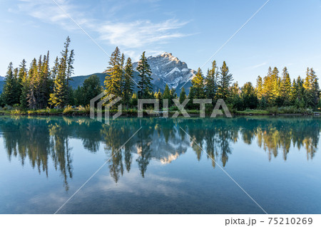 Banff National Park beautiful scenery. Cascade Mountain and pine trees reflected on turquoise color Bow River in summer time. Town of Banff, Canadian Rockies, Alberta, Canada. Banff National Park beautiful scenery. Cascade Mountain and pine trees reflected on turquoise color Bow River in summer time. Town of Banff, Canadian Rockies, Alberta, Canada. 75210269