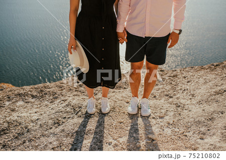Male and female legs in white sneakers on a rock against the sea 75210802
