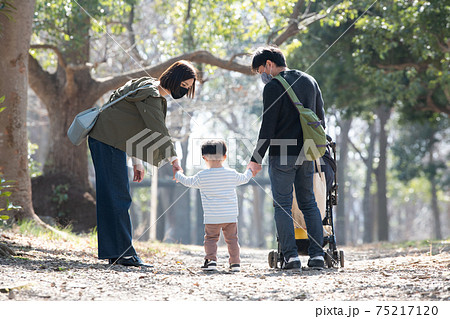 手を繋いで公園を歩く親子の後姿 男の子の子育てをする夫婦の家族イメージの写真素材