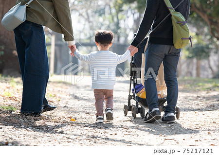 手を繋いで公園を歩く親子の後姿 男の子の子育てをする夫婦の家族イメージの写真素材