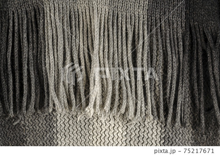 Close-up of fine-checked woolen texture in gray. Winter texture concept, fringe scarf, knitted clothing. Machine knitted woolen goods. Selective focus, noisy texture. 75217671