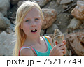 Young blonde girl surprised and holding a seashell 75217749