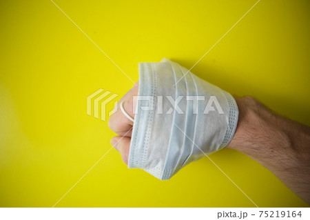 A protective medical mask is wrapped around the arm. The background is made of yellow artistic oil paint. A clenched fist. 75219164