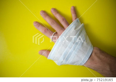 A protective medical mask is wrapped around the arm. Background of yellow artistic oil paint. Mask in hand 75219165