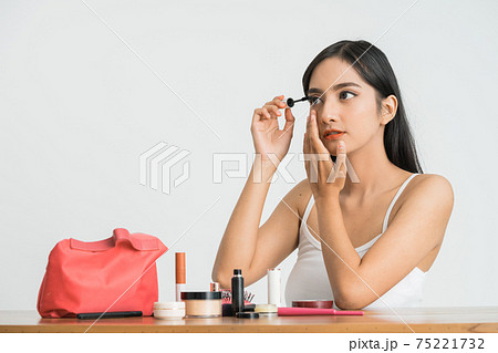 mixed race asian woman putting mascara on eyelashes on white background 75221732