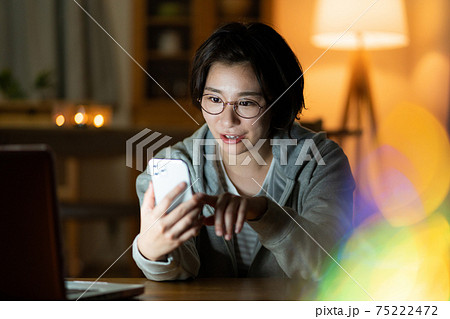 夜リビングでスマホでzoomで会話をする若い女性　 75222472