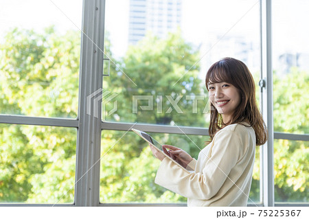 タブレットを持ち窓際に立つ女性 タブレットを持ち窓際に立つ女性 75225367