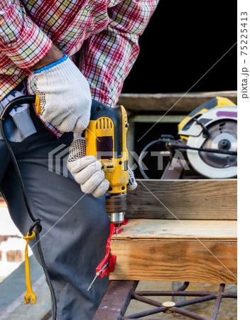 Man drilling a hole in the wooden board. 75225413