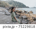 little girl sitting on rock over sea 75229818