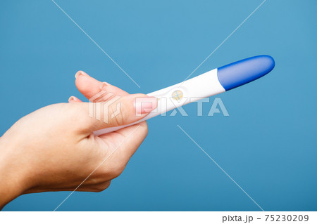 Woman holding holding positive pregnancy test against blue background 75230209