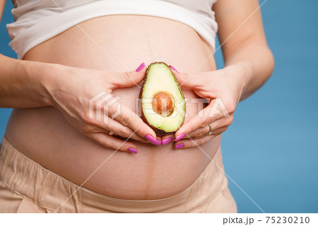 Pregnant woman holding half of avocado next to her belly 75230210