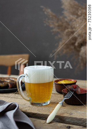 Glass with beer and foam and fork with a piece of sausage 75230366