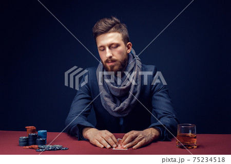 Stylish bearded Man in suit and scarf playing in dark casino, smoking cigar, drink whiskey Stylish bearded Man in suit and scarf playing in dark casino, smoking cigar, drink whiskey 75234518