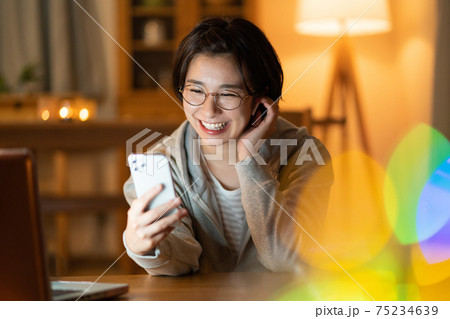 夜リビングでスマホでzoomで会話をする若い女性　 75234639