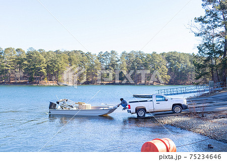 Pickup truck pulling boat and trailer out of the water at the shore of a lake.. Pickup truck pulling boat and trailer out of the water at the shore of a lake.. 75234646