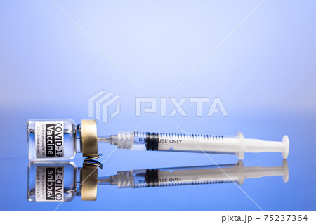 Syringe inserted into vial containing Covid-19 vaccine concept on blue background 75237364