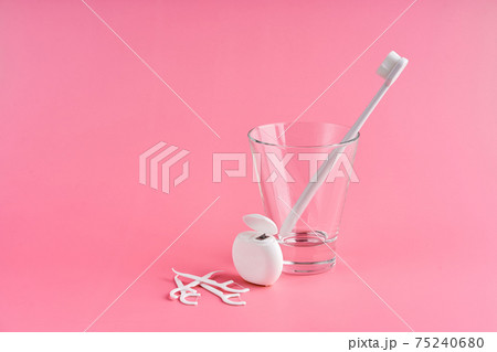 Fashionable toothbrush with soft bristles. Popular toothbrushes. Hygiene trends. Oral hygiene kit. Toothbrushes in glass, floss thread and toothpicks on a pink background 75240680