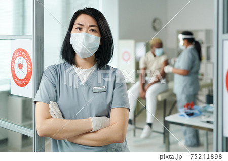 Young cross-armed female clinician in protective workwear standing in front of camera 75241898