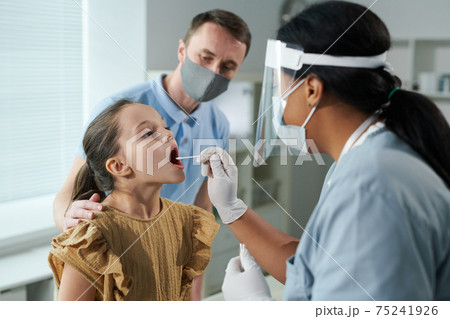 Little girl sitting in front of nurse testing her for covid with cotton bud 75241926