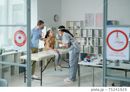 Little patient with open mouth being tested for covid by young female clinician Little patient with open mouth being tested for covid by young female clinician 75241929