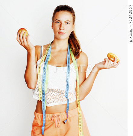 young blonde woman choosing between donut and apple fruit isolated, holding measurment tape 75242957