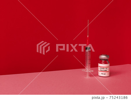 Medical bottle with covid 19 vaccine and syringe on red backdrop with tilted trendy skyline and copy space. Medical bottle with covid 19 vaccine and syringe on red backdrop with tilted trendy skyline and copy space. 75243186