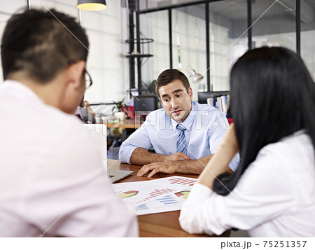 two asian business executives discussing business performance with caucasian superior in office two asian business executives discussing business performance with caucasian superior in office 75251357