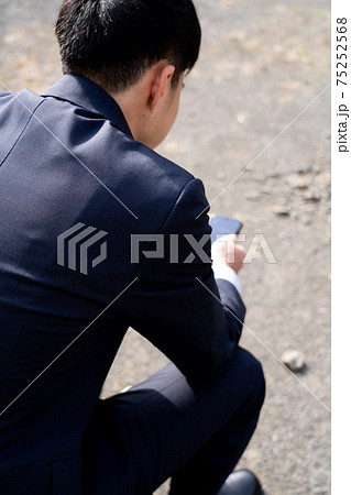 スーツを着ている男性が公園のベンチに座ってスマートフォンを見ているの写真素材