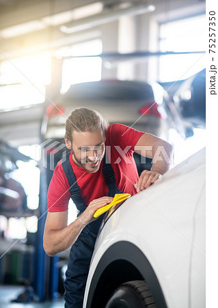 Joyful repairman wiping car clean with napkin Joyful repairman wiping car clean with napkin 75257350