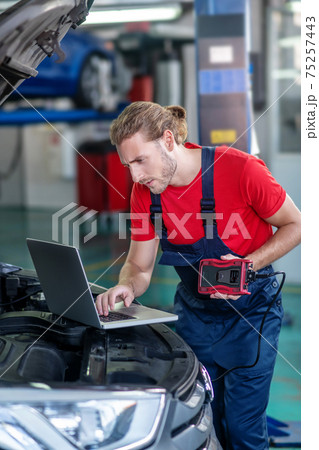 Interested repairman with computer near the car Interested repairman with computer near the car 75257443