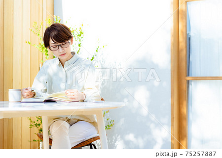テラスで読書をする眼鏡をかけたミドルの女性 テラスで読書をする眼鏡をかけたミドルの女性 75257887