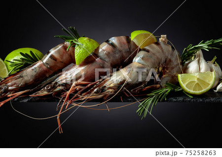 Fresh tiger prawns with lime, rosemary and garlic on a black background. Fresh tiger prawns with lime, rosemary and garlic on a black background. 75258263