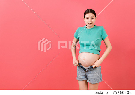 pregnant woman in unzipped jeans showing her naked abdomen at colorful background with copy space pregnant woman in unzipped jeans showing her naked abdomen at colorful background with copy space 75260206