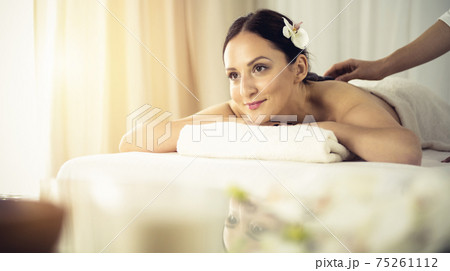 Pretty brunette woman enjoying treatment with hot stones in spa salon. Beauty concept Pretty brunette woman enjoying treatment with hot stones in spa salon. Beauty concept 75261112