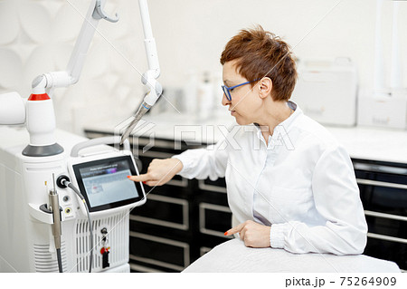 Cosmetologist near laser treatment device in beauty clinic. 75264909