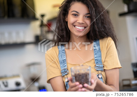 Smiling woman holding out glass of coffee beans 75265786