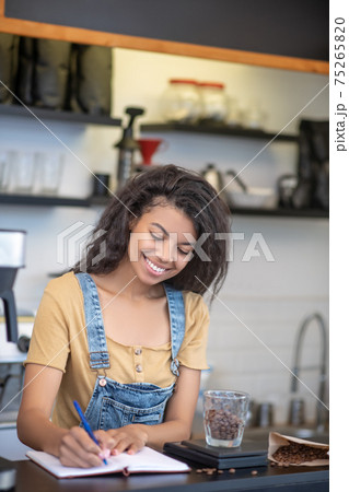 Cheerful woman writing weight of coffee beans in notebook 75265820