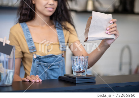 Female hand pouring coffee beans into measuring cup 75265860
