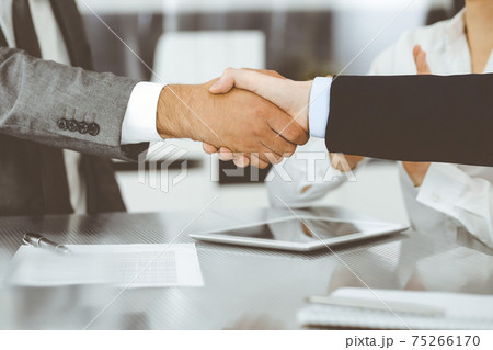 Handshake as successful negotiation ending, close-up. Unknown business people shaking hands after contract signing in modern office Handshake as successful negotiation ending, close-up. Unknown business people shaking hands after contract signing in modern office 75266170