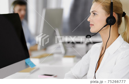 Blonde business woman using headset for communication and consulting people at customer service office. Call center. Group of operators at work 75266777